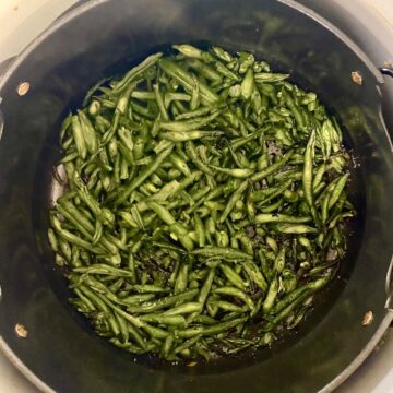 Cooked frozen green beans in the air fryer basket of a ninja foodi.