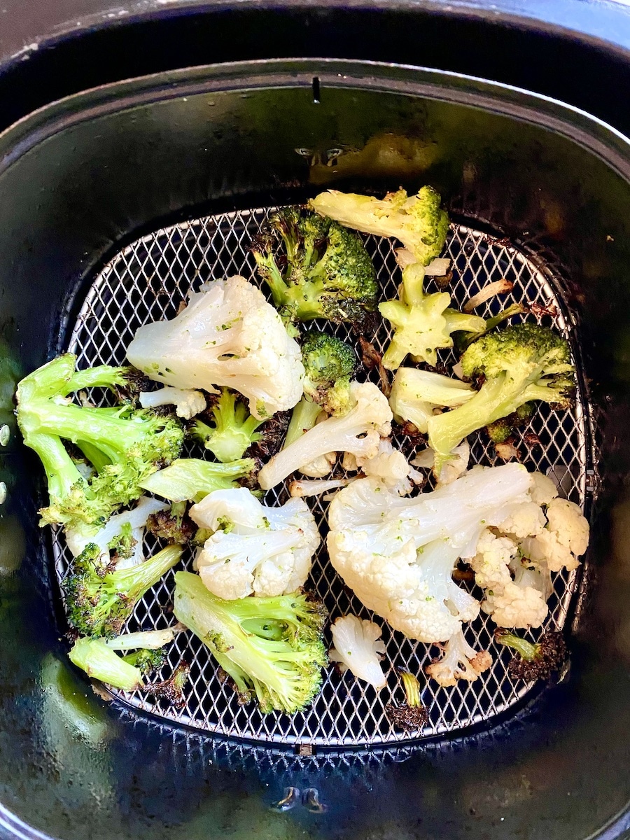 Cooked air fryer broccoli and cauliflower in a air fryer basket
